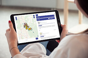 Frau von hinten, die ein Tablet in der Hand hält, auf dem die Webseite der ersten Online-Beteiligung zum nachhaltigen Mobilitätsplan Weinheim 2040 dargestellt ist.